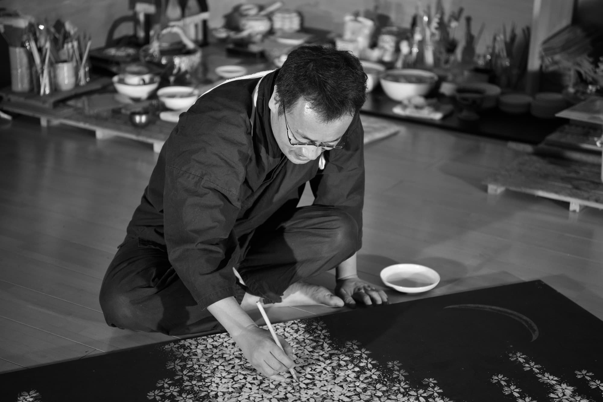 Hiromitsu Kato pintando pétalos de cerezo sobre un biombo dispuesto en el suelo