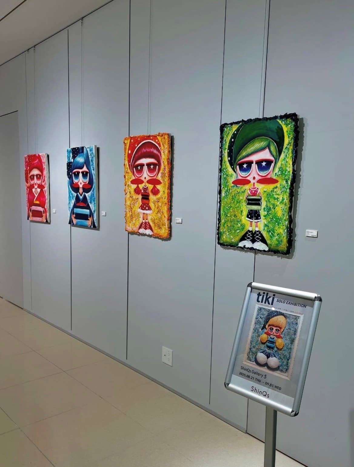 Works on a grey wall, with the exhibition sign